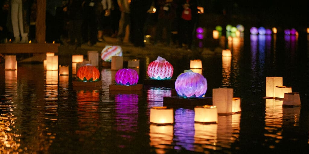 Sedona Lantern Festival – Floating Lanterns at Night Colorful lotus lanterns and glowing paper lights floating on the water during Sedona Mago’s annual lantern festival, with people gathered along the shore.