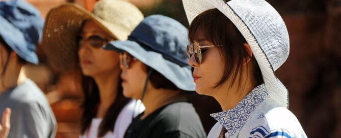 Group of people wearing sun hats and sunglasses meditating outdoors in bright desert sunlight.