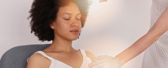 Practitioner’s hands positioned over a woman’s chest as she meditates with eyes closed during a calming energy healing session.